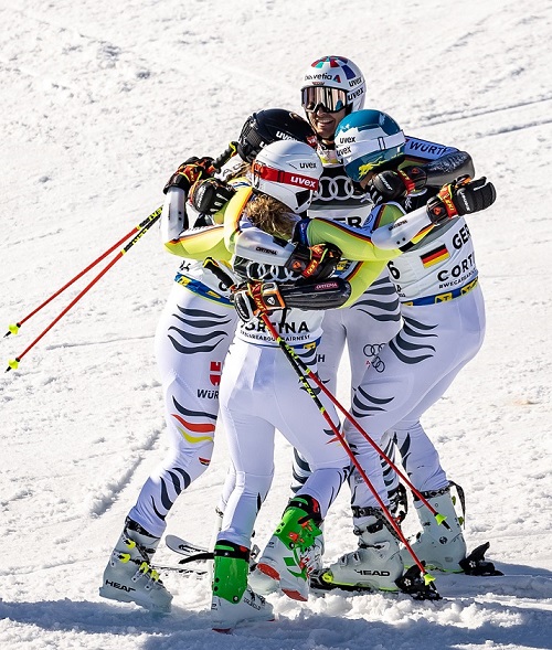 Team of four skiing hugging each other and all wearing helmet and ski goggles from uvex.