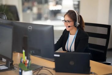 Auszubildende für Büromanagement sitzt mit Headset am Schreibtisch und telefoniert.