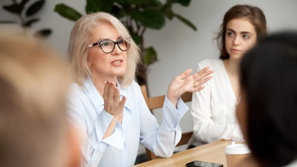 Woman leading a meeting in a modern office, gesturing while speaking as colleagues listen attentively