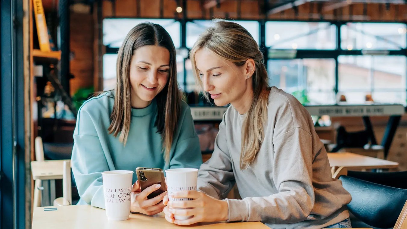 esm-customer-service-two-women-in-cafe-looking-at-phone