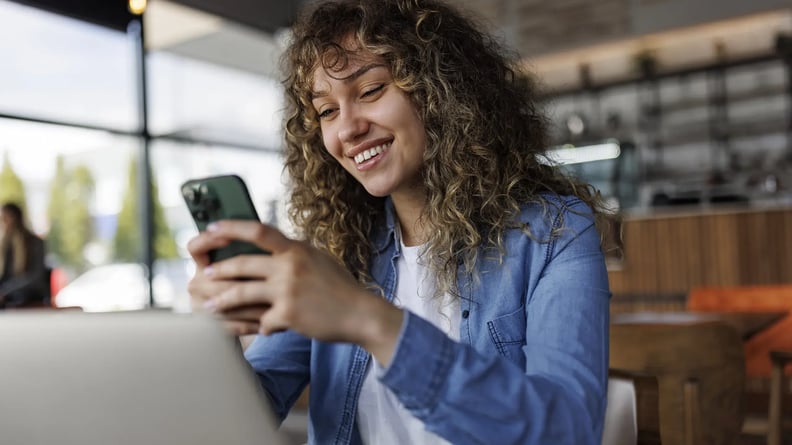 esm-customer-service-woman-in-cafe-smiling-at-phone-with-laptop