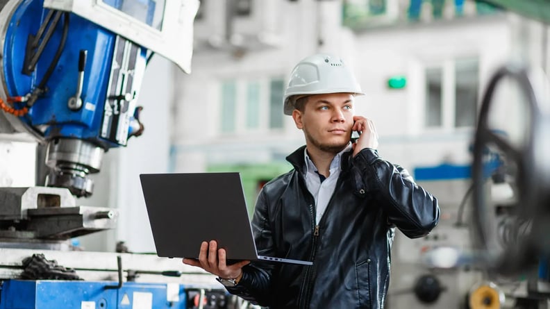 esm-field-service-man-in-factory-helmet-on-phone-with-laptop