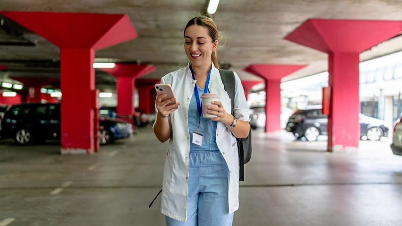 esm-healthcare-nurse-outside-parking-garage-walking-looking-at-phone