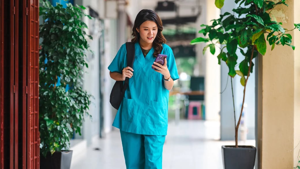 esm-healthcare-nurse-walking-outside-looking-at-phone