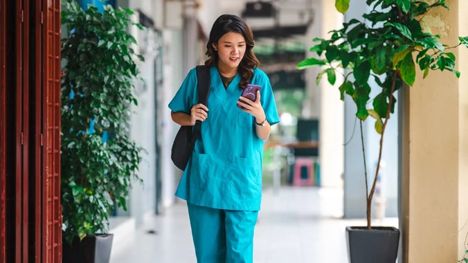 esm-healthcare-nurse-walking-outside-looking-at-phone