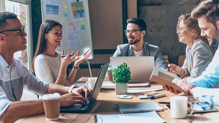 Vijf marketingcollega's zitten aan een groot bureau en bespreken een campagne.