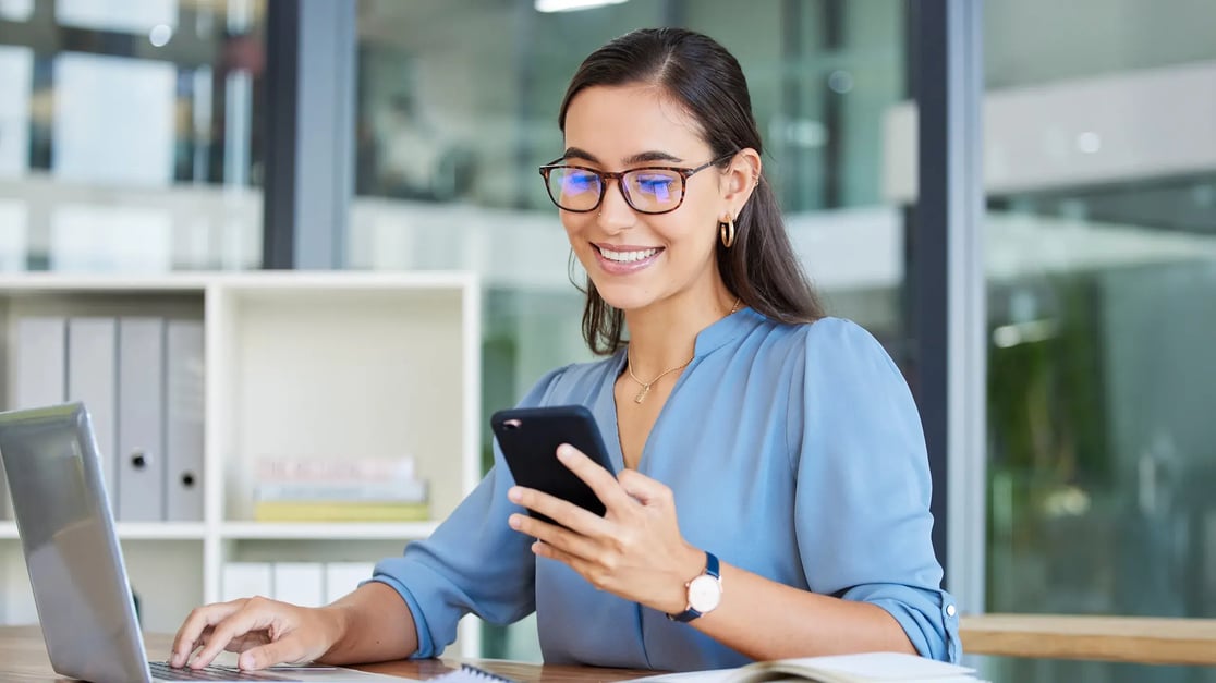 esm-itsm-woman-on-laptop-checking-phone-smiling