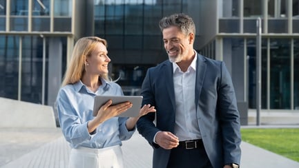Business professionals walking outside a modern office building, discussing work while reviewing a tablet