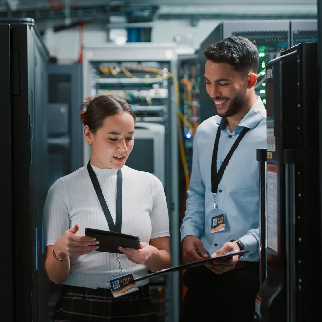 IT professionals discussing work in a server room, reviewing information on a tablet among network equipment