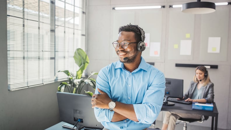 Businessmann im Büro mit Headset, im Hintergrund eine arbeitende Kollegin