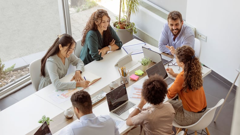 Menschen tauschen sich an einem Tisch mit Laptops in einem Büro aus