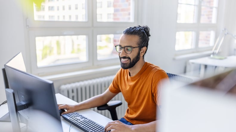 Eine Person arbeitet in einem hellen Raum und blickt erfreut auf den Bildschirm