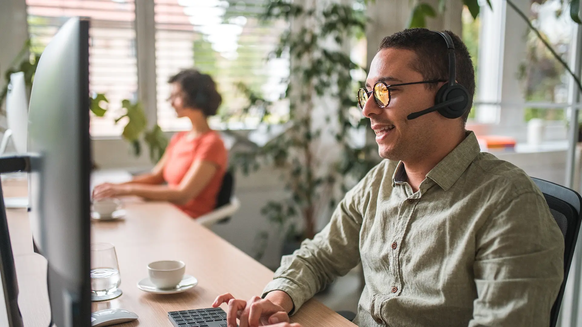 Mann mit Brille kommuniziert ueber Headset am Arbeitsplatz