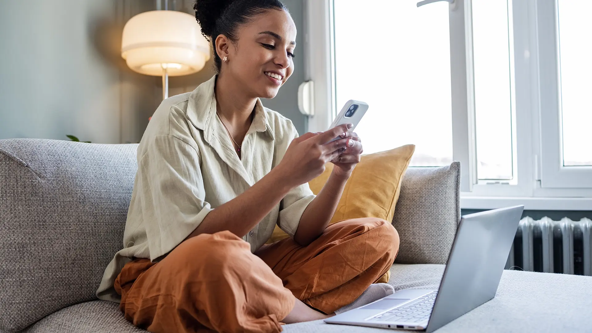 woman sitting at home using smartphone and laptop